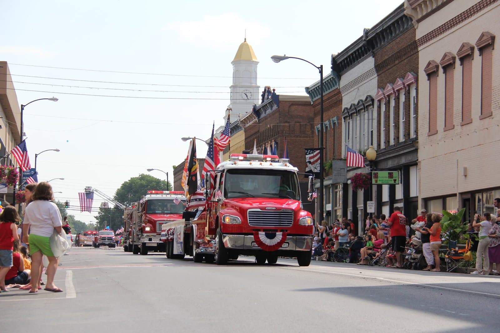 Small-town Kentucky parade with fire trucks rolling down a flag-lined Main Street past the courthouse