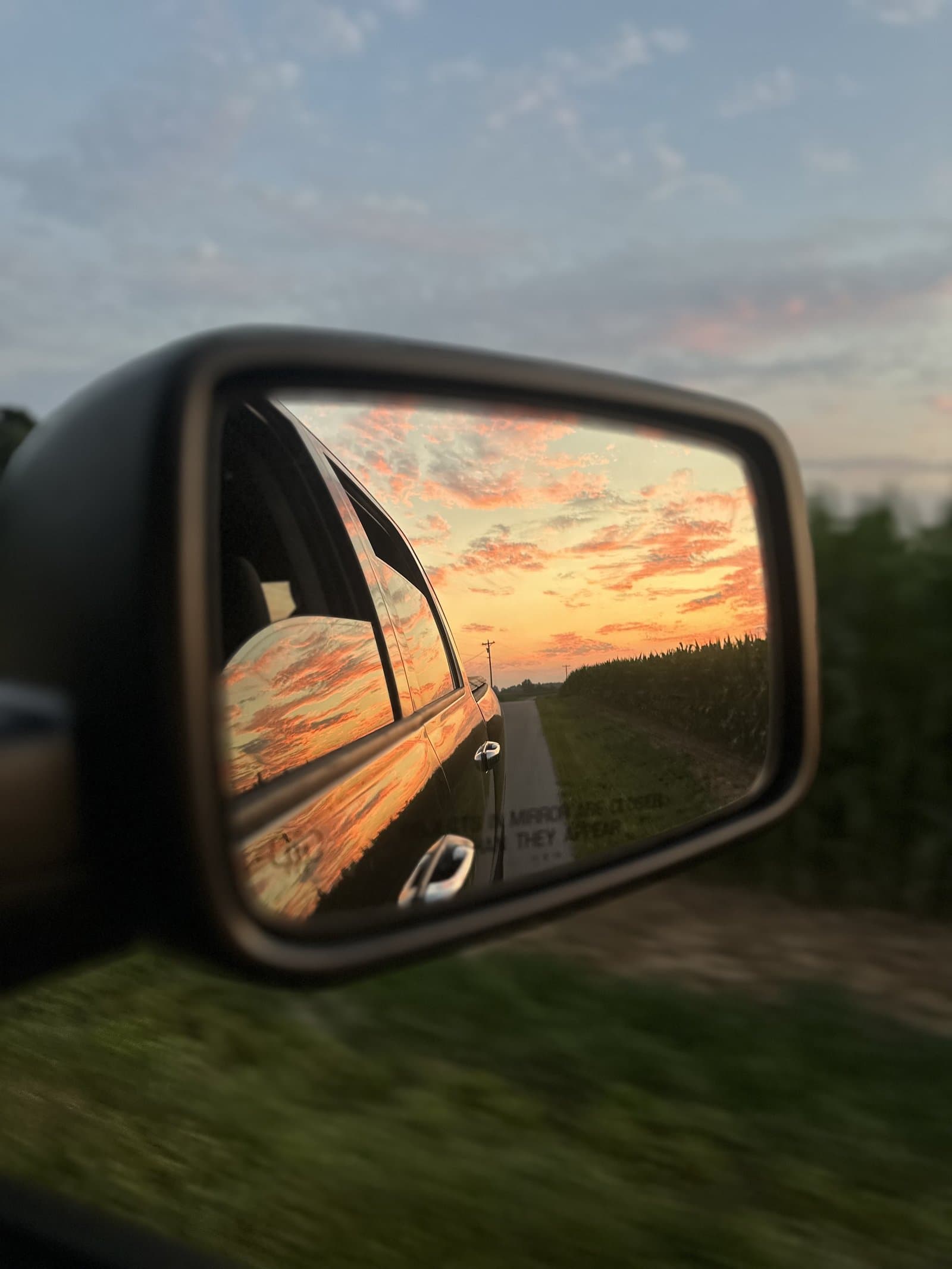 Kentucky sunset reflected in a car's side mirror, country road stretching ahead through cornfields