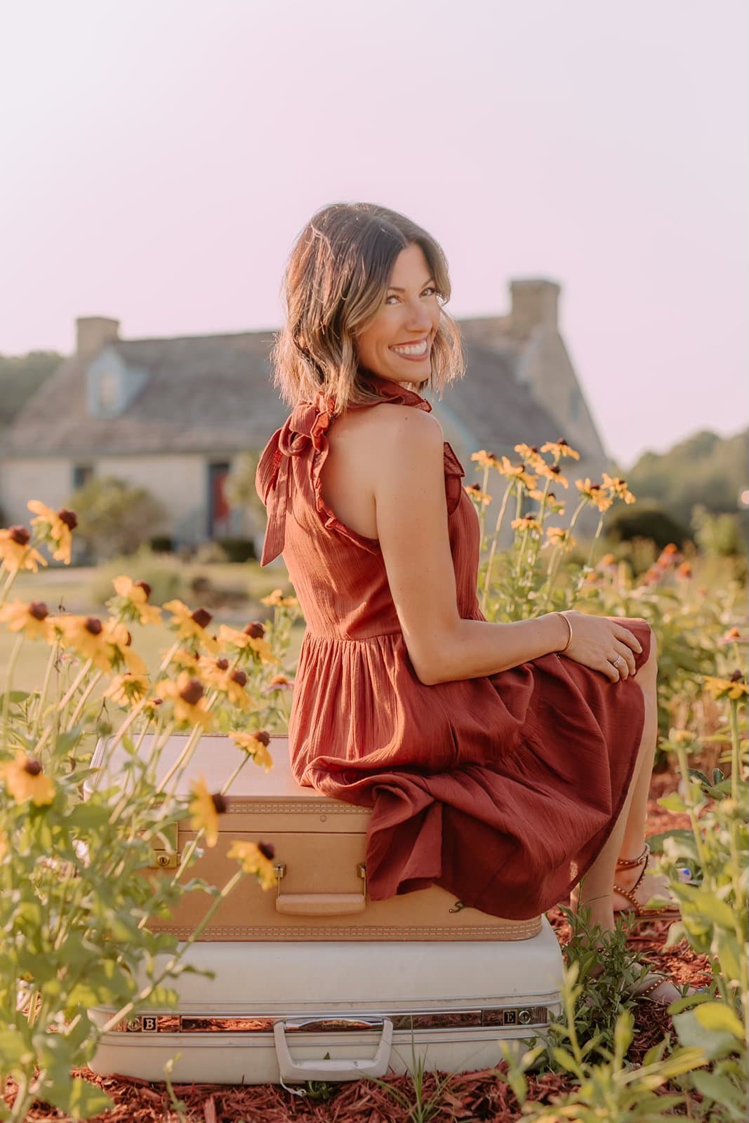Lindsey, founder of You + Me Kentucky, sitting on vintage suitcases in a field of black-eyed Susans